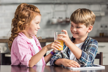 happy little sister giving glass of orange juice to her brother