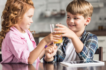 little brother and sister passing glass of orange juice at kitchen