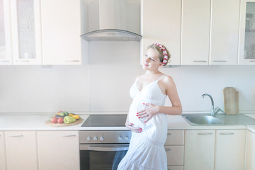 pregnant woman in the kitchen in a white dress.