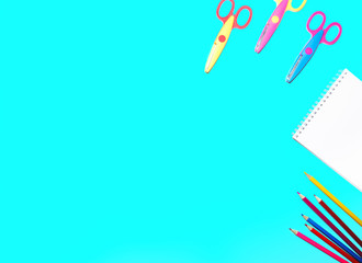picture of colored pencils, notepad and scissors lined on a flat surface of an isolated blue background