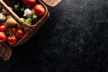 flat lay with various fresh vegetables in basket on black marble tabletop