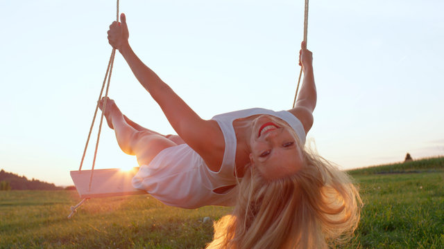 SLOW MOTION CLOSE UP: Happy young woman smiles and leans back on swing in nature