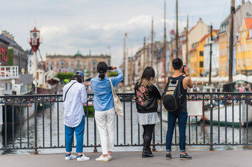 Tourists enjoying the scenic summer view of Nyhavn pier. Colorful building facades with boats and yachts in the Old Town of Copenhagen, Denmark
