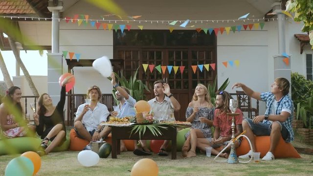 Happy group of people having fun, smiling, enjoying picnic party with drinks and fruits outdoors together. Young friends celebrating birthday. Holiday celebration festive party. Teenage lifestyle.