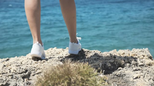 Close-up girl's lags walk on stone cliff at sea. 4K
