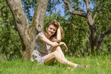 Naklejka na ściany i meble Young cute woman sits and rests in the garden under a tree