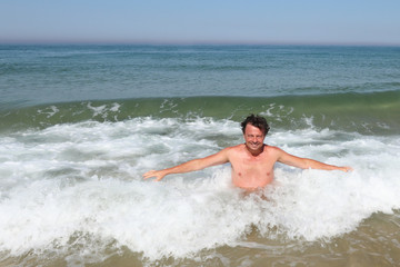 man bathes on the beach as ocean waves crash behind him