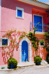Fototapeta na wymiar Assos village. Traditional pink colored greek house with bright blue door and windows. Fucsie plant flowers arount entrance welcome gate. Kefalonia island, Greece