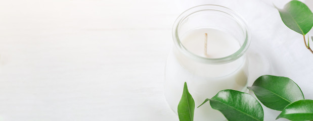 Long Banner for Organic Cosmetics Wellness White Candle in Glass Jar Fresh Tree Branches with Green Leaves on Wood Background. Spa Body Care Meditation Purity Concept. Minimalist Style. Copy Space
