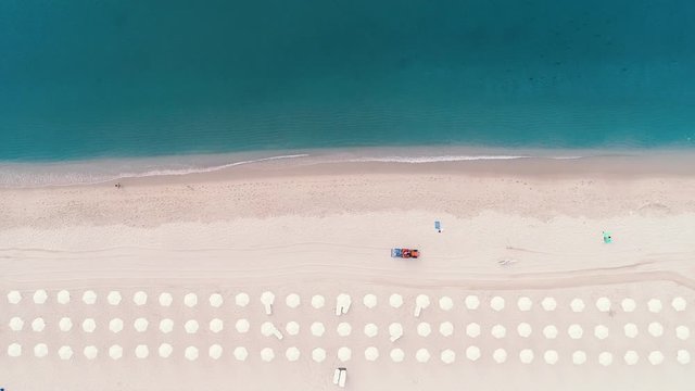 Aerial top view on the beach. Umbrellas, sand and sea waves. Working sand cleaning machine.