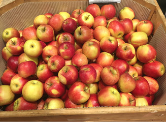 a lot of red apples in wooden box and brown paper in supermaket for sell.