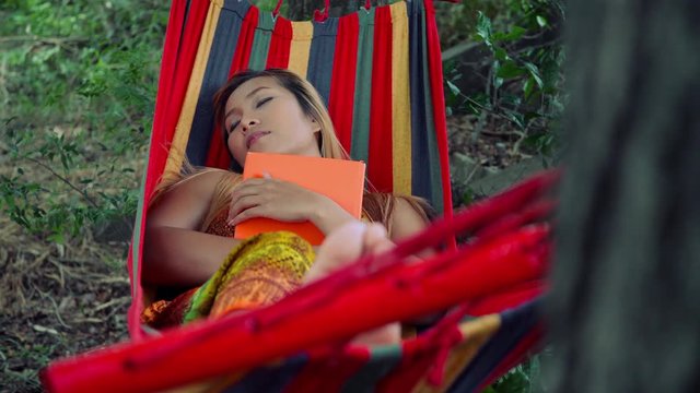 Young woman laying down on hammock and reading a book