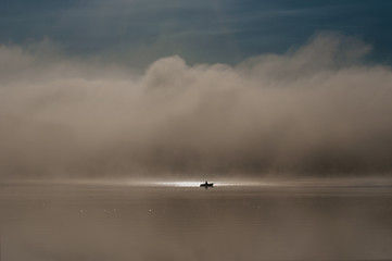 Fototapeta na wymiar Mglisty krajobraz nad jeziorem i czlowiek na łódce