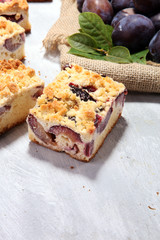 Rustic plum cake on wooden background with plums around.