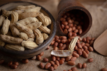 Peanuts in nutshell on a piece of wooden bowl and peeled peanuts on sackcloth