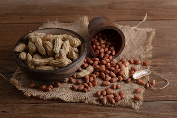 Peanuts in nutshell on a piece of wooden bowl and peeled peanuts on sackcloth