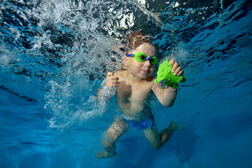 A little boy playing underwater in the pool. It floats and spins among the air bubbles on a blue...