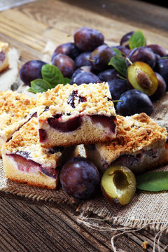 Rustic plum cake on wooden background with plums around.