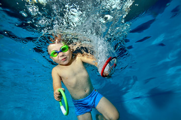 Happy kid doing sports and swimming underwater in the pool on a blue background with toys in his...