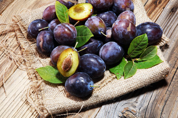 Plums on rustic background. Half of blue plum fruit. Many beautiful plums with leaves