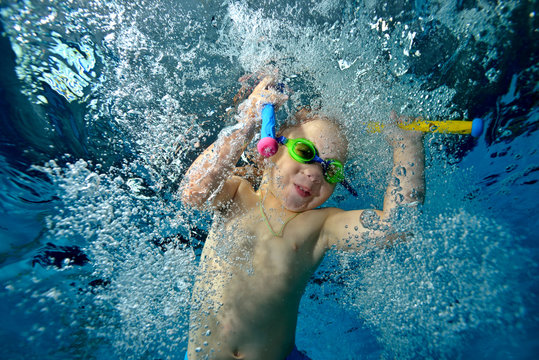 Underwater photography. A little boy plays and swims underwater in the pool with toys in his hands in bubbles. Portrait. Bottom view. The horizontal orientation of the image