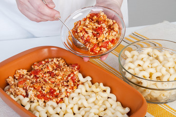The cook prepares a meat casserole with pasta.