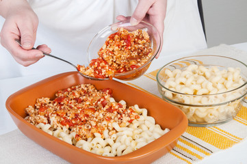 The cook prepares a meat casserole with pasta.