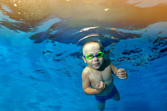 A little boy swims and poses under the water in the children's pool on the background of yellow lights. Portrait. Underwater photography. The horizontal orientation of the image