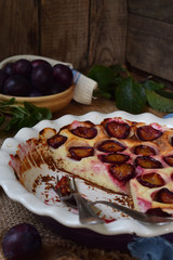 Plum pie in white ceramic form on a wooden background. Homemade baking. Healthy pastries. Vegetarian food. Rustic photo. Copy space.
