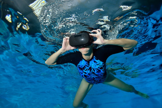 Virtual reality simulator. An unusual girl swims underwater in the pool in black virtual reality glasses on her head. Shooting underwater. Horizontal orientation