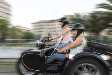 Two happy sister blonde women on sidecar bike smiling and happy