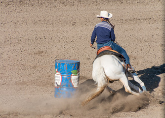 Barrel Racing A cowgirl with long blond braid, white hat and blue shirt rides on the back of a...