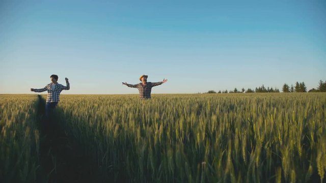 Happy father and son walking on wheat field, rejoicing with outstretched arms