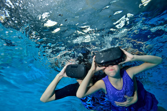 Virtual reality. A little girl with her mother in a virtual reality helmet on her head floats from the bottom to the surface underwater. Bottom view. Underwater photography