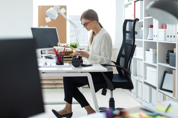 A young girl sits at a table in the office and holds a yellow marker in her hand. Before the girl lies an open book.