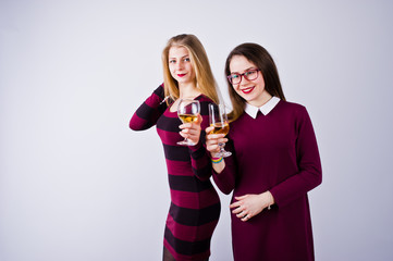 Two attractive friends in purple dresses drink sparkling wine or champagne in the studio.