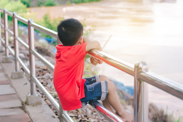 Naklejka premium Kid boy sit on the iron balcony,looking the river.