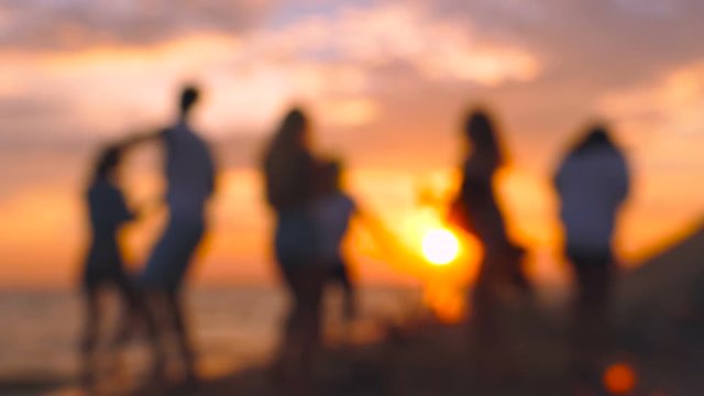 Blurred footage of group of people dancing during the sunset on the beach.  