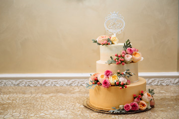 Golden wedding three-story cake. Close-up of a delicious dessert decorated with flowers, wedding cake decor. Copy space
