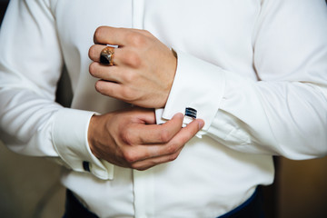 Obraz na płótnie Canvas A man in a business suit, white shirt close-up of a cropped frame. The businessman puts on cufflinks, wears a gold finger ring on his finger, an expensive leather belt.