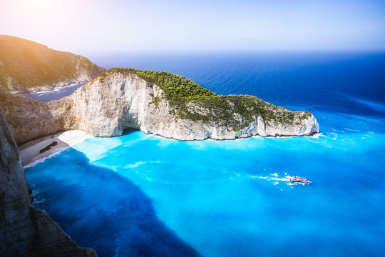 Navagio beach, Zakynthos island, Greece. Tourist trip boat leaving Shipwreck bay with deep turquoise water and white sand beach surrounded by bizarre cliff rocks. Famous landmark location