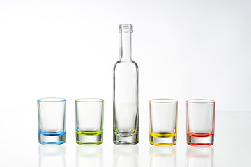 Four multicolored empty shot glasses and small bottle placed symmetrically on a white background.