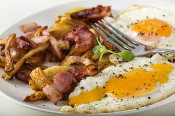 Homemade eggs with French fries and fried bacon on plate