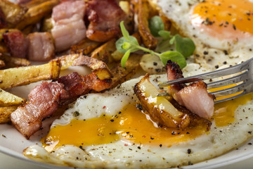 Homemade eggs with French fries and fried bacon on plate
