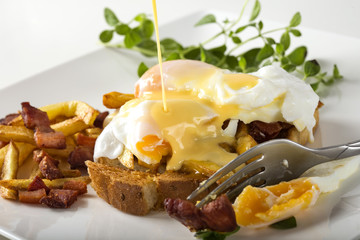 Toast sandwich with two poached eggs, French fries and bacon