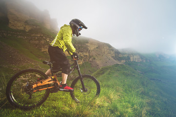 Fototapeta premium A man in a mountain helmet riding a mountain bike rides around the beautiful nature in cloudy weather. downhill