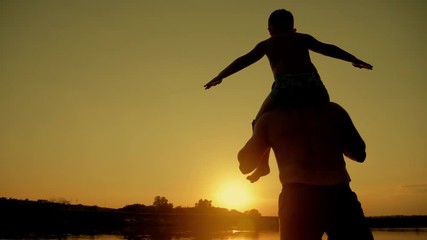 father and son silhouettes playing on beach boy rising up hands imitating a flight at wonderful sunset through the shining sun happy family concept of a united family - Powered by Adobe