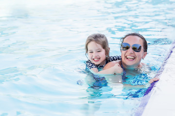 Summer holiday concept. Happy mother and her little daughter playing in swimming pool