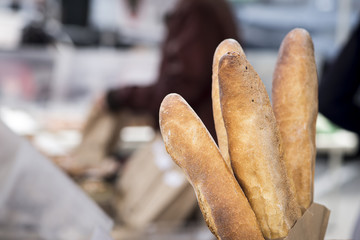 Baguettes on sale at a market.  Shoppers out of focus in the background.