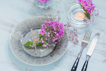 Rustic table setting with pink flowers and candle on light wooden table.